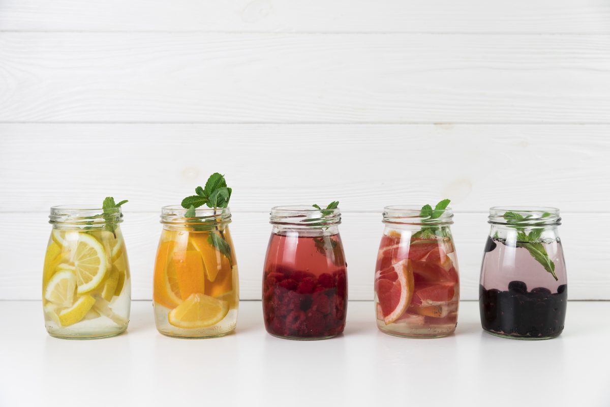 Lima toples berisi infused water dari lemon, jeruk, raspberry, grapefruit, dan blueberry dengan daun mint sebagai minuman detoks alami.