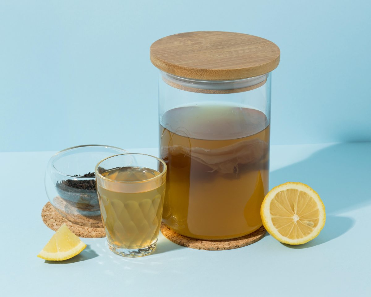 Segelas kombucha dengan irisan lemon segar dan daun teh hitam sebagai bahan utama minuman detoks alami.