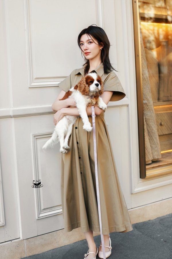 Orm Kornnaphat memegang anjing kecil sambil mengenakan long dress krem Dior di depan butik Dior Paris